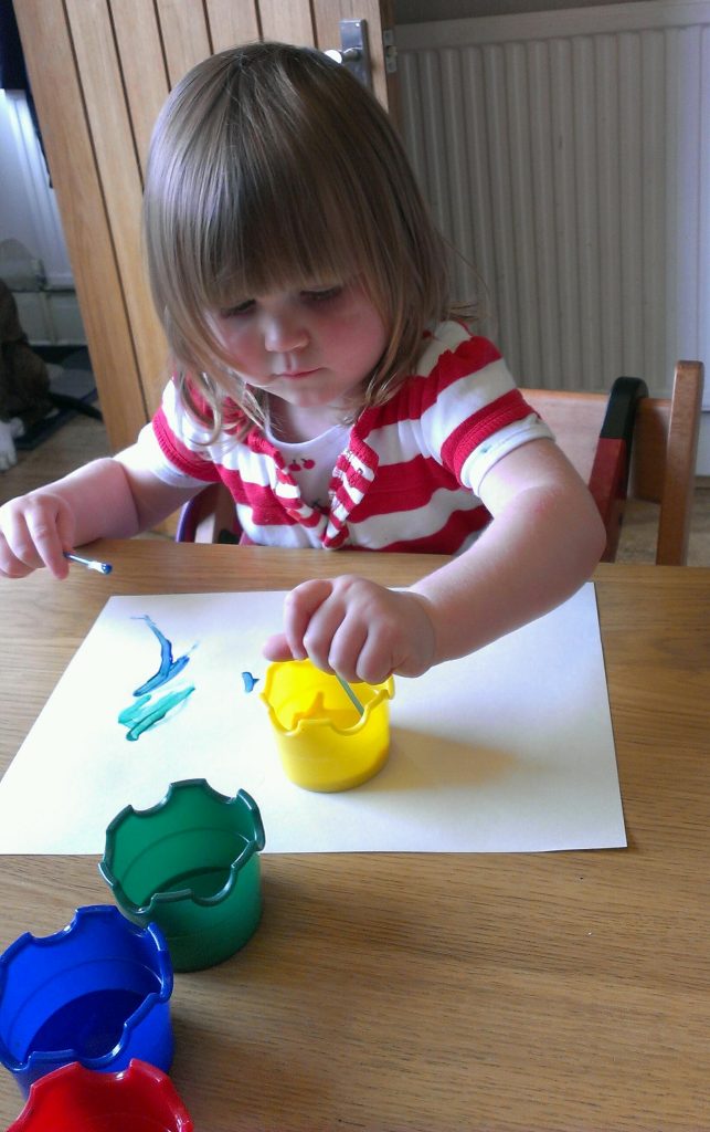 Little girl painting with poster paint and cotton buds