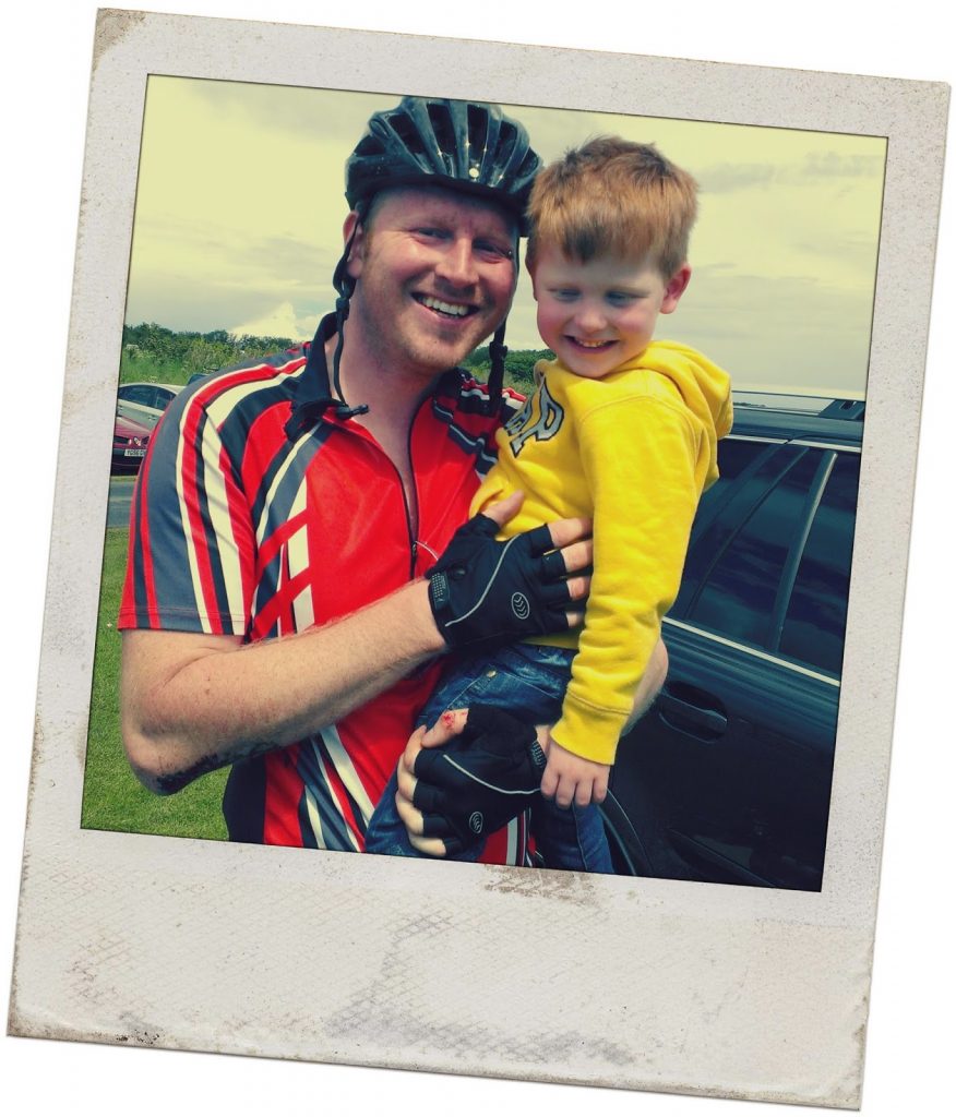 Man wearing cycling gear and holding his young son