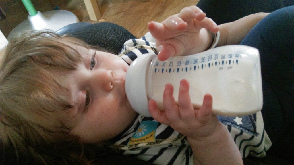 little girl learning to drink from her bottle - moving from breast to bottle