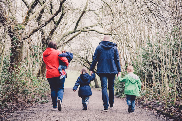 Family of five walking away from the camera - Dad holding hands with two children and Mum carrying the youngest - photo taken by Sally Langstaff