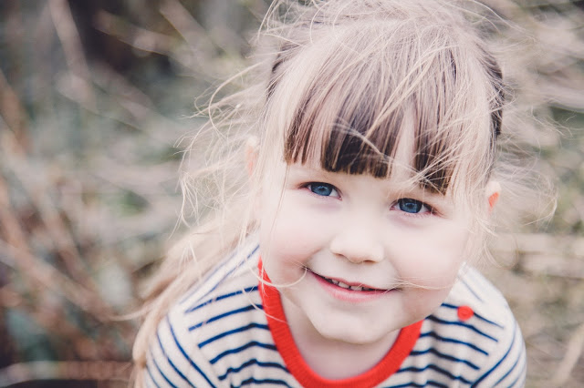 Little girl with heavy fringe and blue eyes wearing a navy stripe top with red detail - photograph by Sally Langstaff