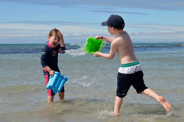 Little boy throwing a bucket of seawater in his little sister's face