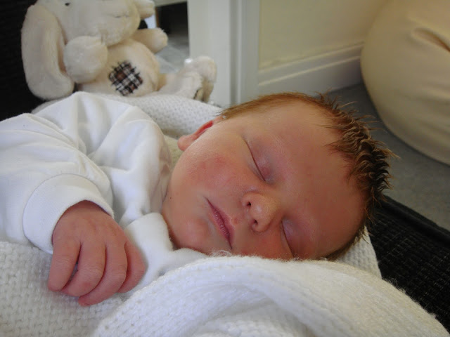 Tiny new born baby boy tucked up in a white, hand-knitted blanket washed in Comfort Pure