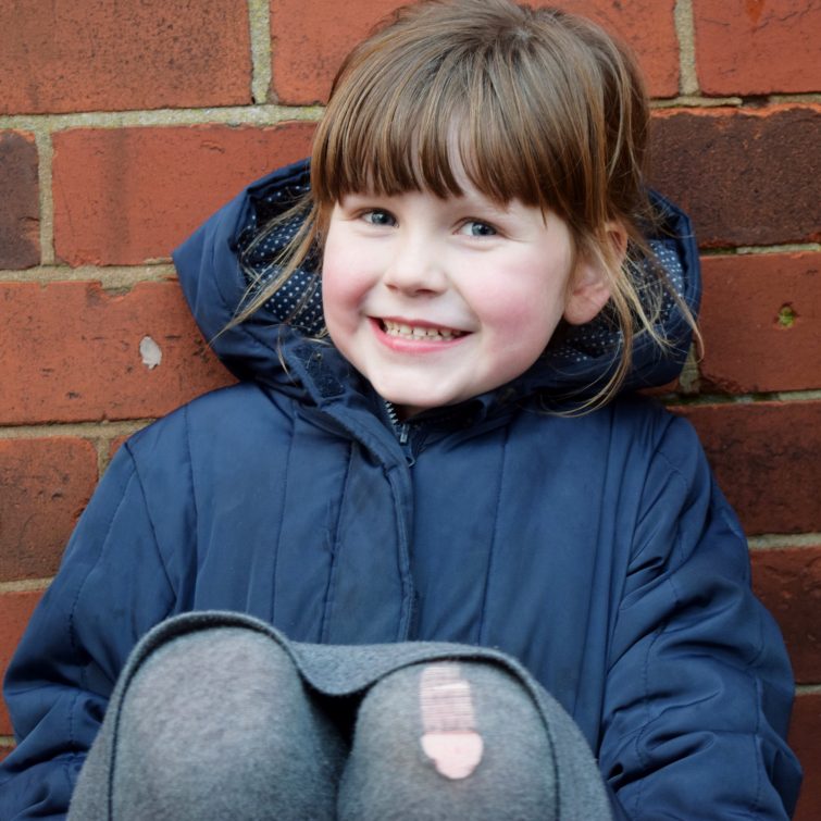 Little girl wearing her school coat and ripped tights