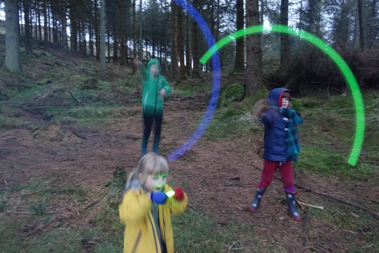 Children spinning glow sticks on a spring in the woods