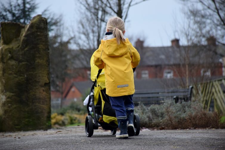Little girl pushing her dolls in her yellow pushchair