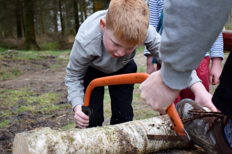 Young boy chopping wood for the fire with a saw