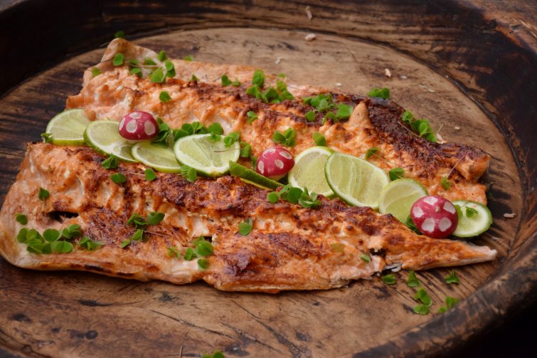 fresh whole salmon cooked on an open fire, served on a wooden platter