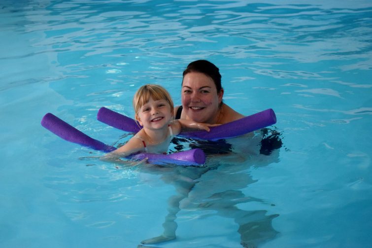 Toddler swimming with woggles in her Puddle Ducks lesson