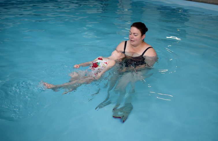 Little girl swimming on her back with her mum's help