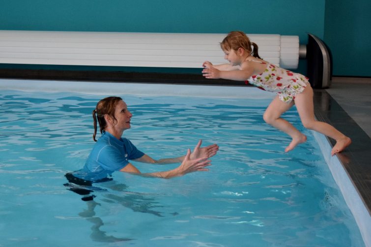 Little girl jumping into the pool to her swimming teacher