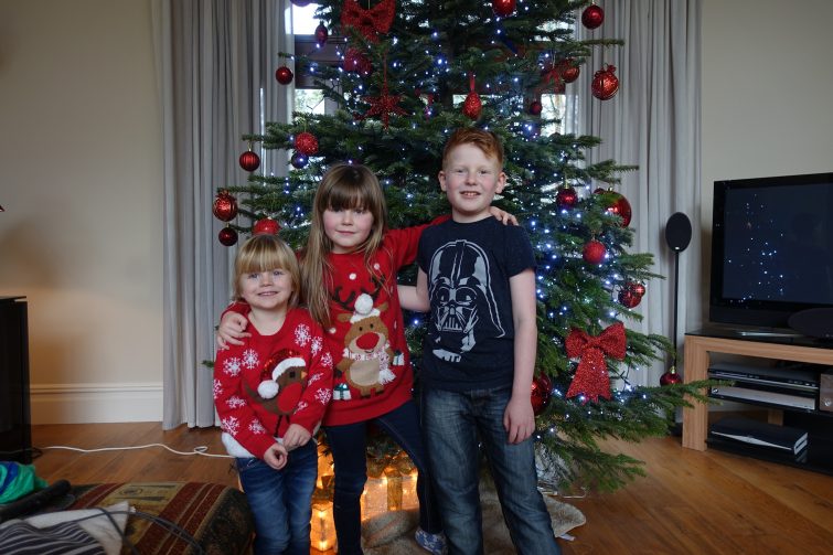 Children standing in front of a large Christmas tree decorated with red baubles