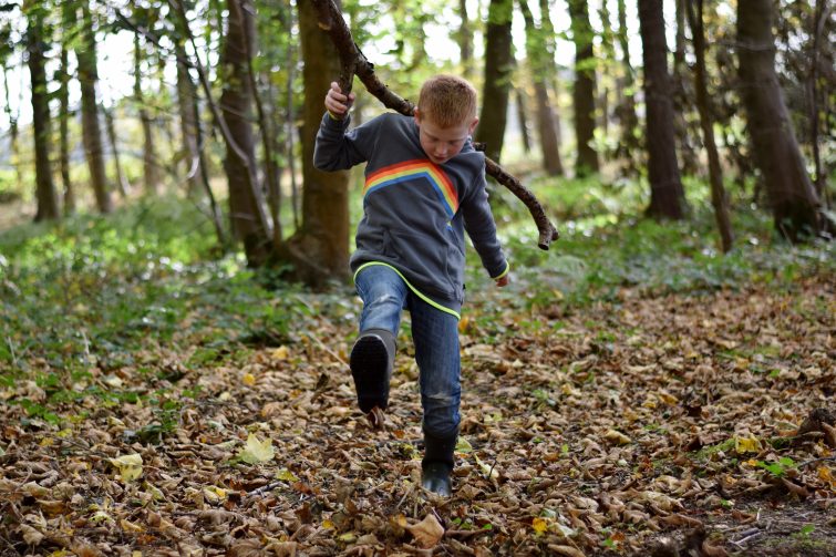little boy kicking leaves in the woods wearing his bogs boots