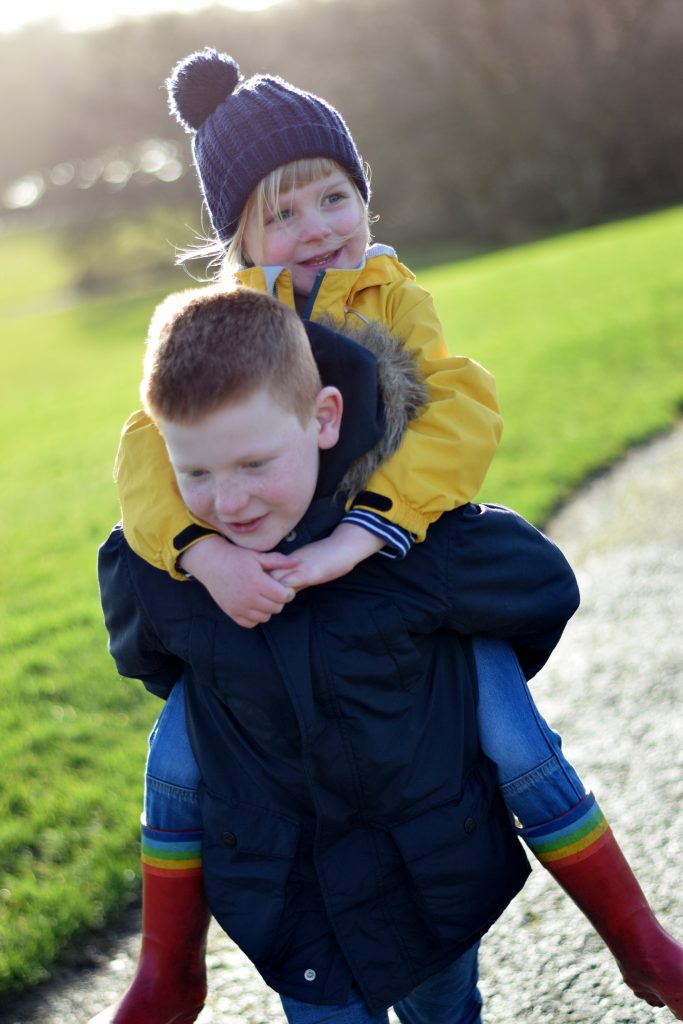 Big brother giving his little sister a piggyback in the park
