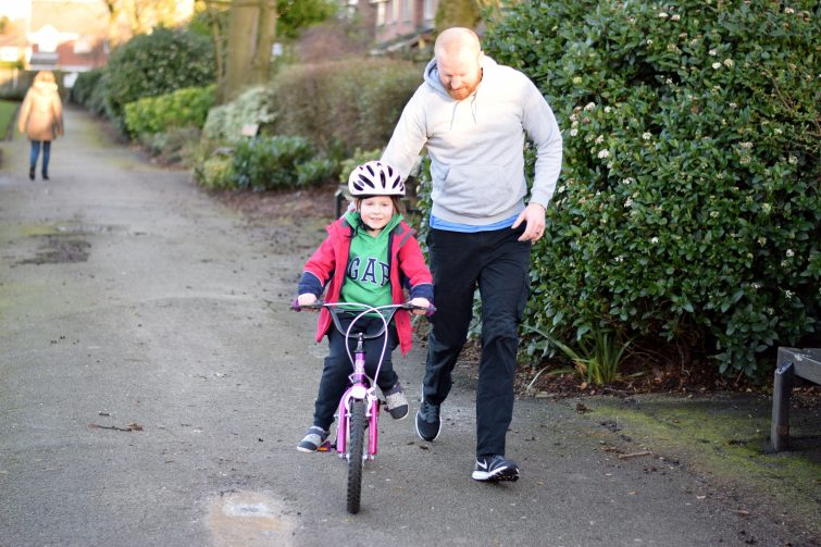 Little girl learning to ride a bike with Daddy running alongside her
