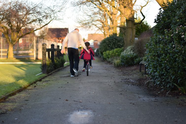 Daddy with one hand on his daughter's back as she learns to ride a bike