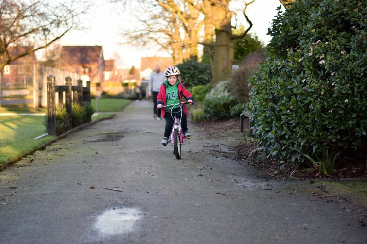 Learning to ride a bike - success as little girl rides by herself while Daddy watches proudly