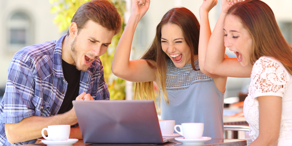 A group of young friends cheering at a laptop after winning.