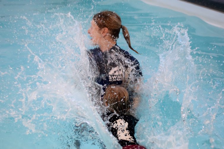Swim Academy / Puddle Ducks pyjama week - little girl jumping into the pool in her pjs and splashing her teacher
