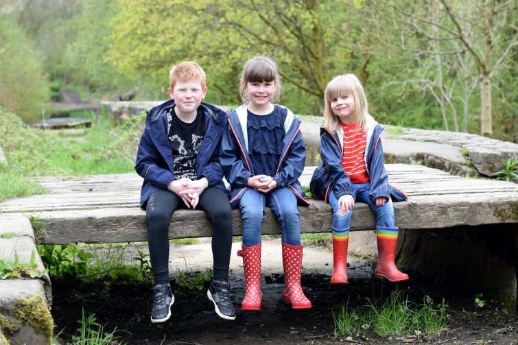 Three siblings sitting on a wooden bench over a disused canal