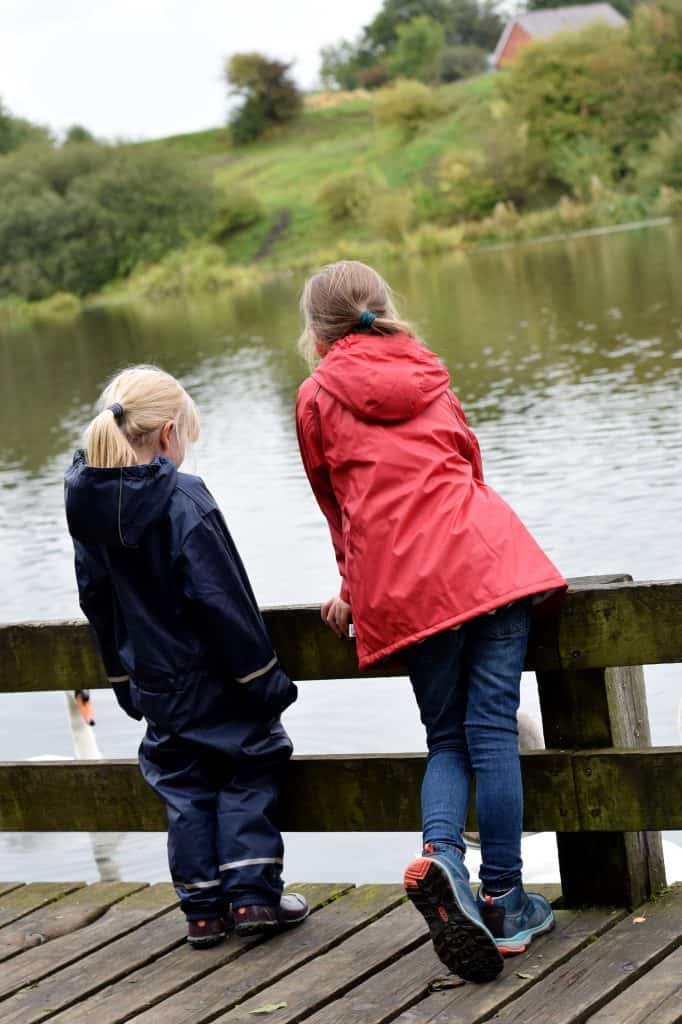 Little girls looking out at the lake wearing Muddly Puddles coat / puddle suit
