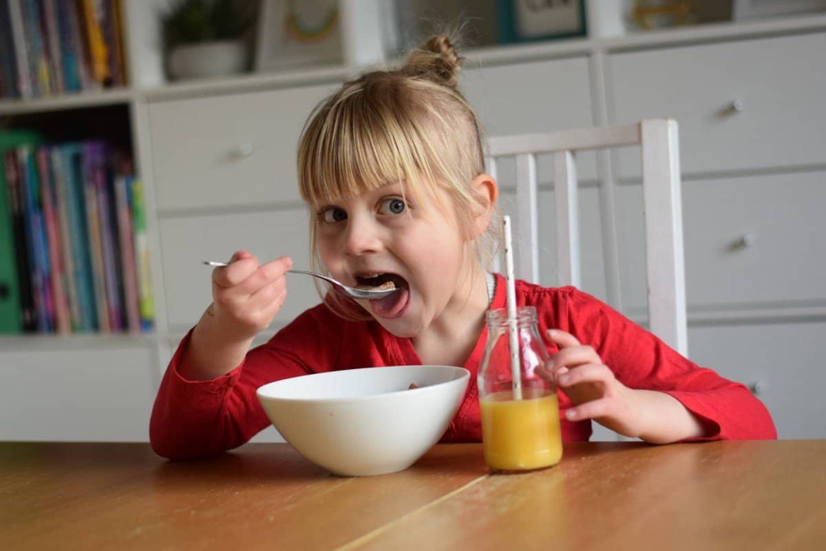 little girl eating breakfast cereal with orange juice