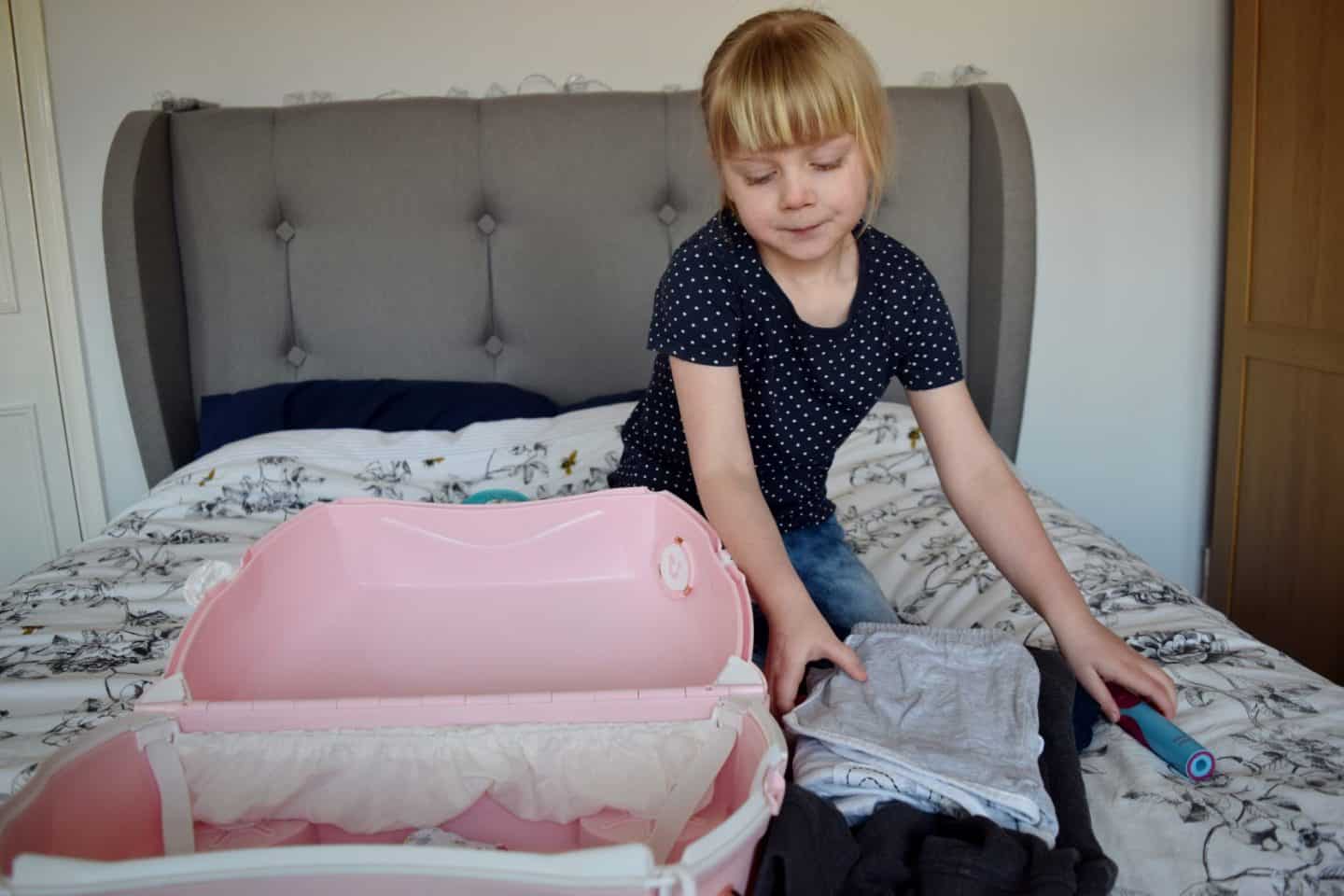 Little girl packing her own Trunki suitcase for a weekend away