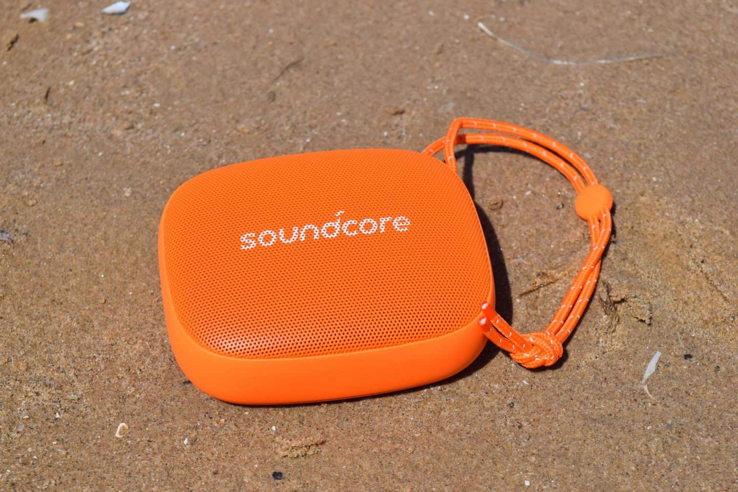 Bright orange Soundcore Icon Mini bluetooth speaker on the beach