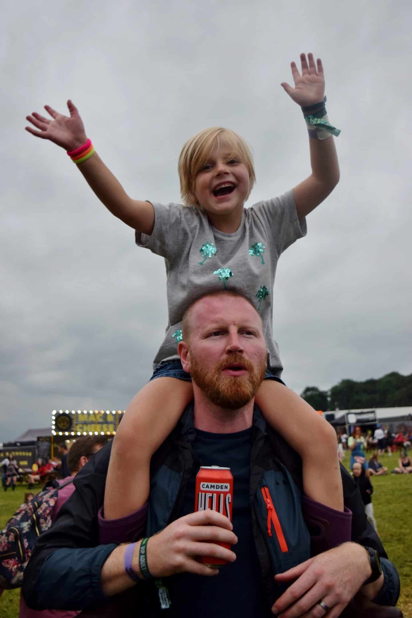 Little girl sat on her Dad's shoulders at a festival