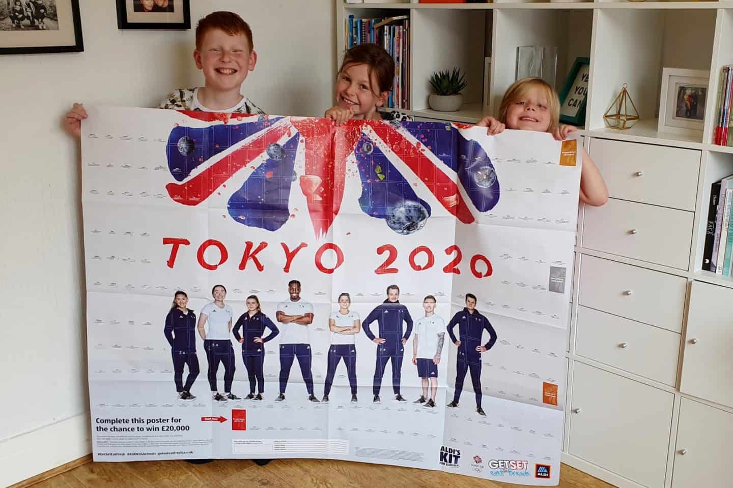 Children showing off the Aldi Kit for Schools poster - schools need to collect stickers and add to this poster to earn a Mini Olymics Kit