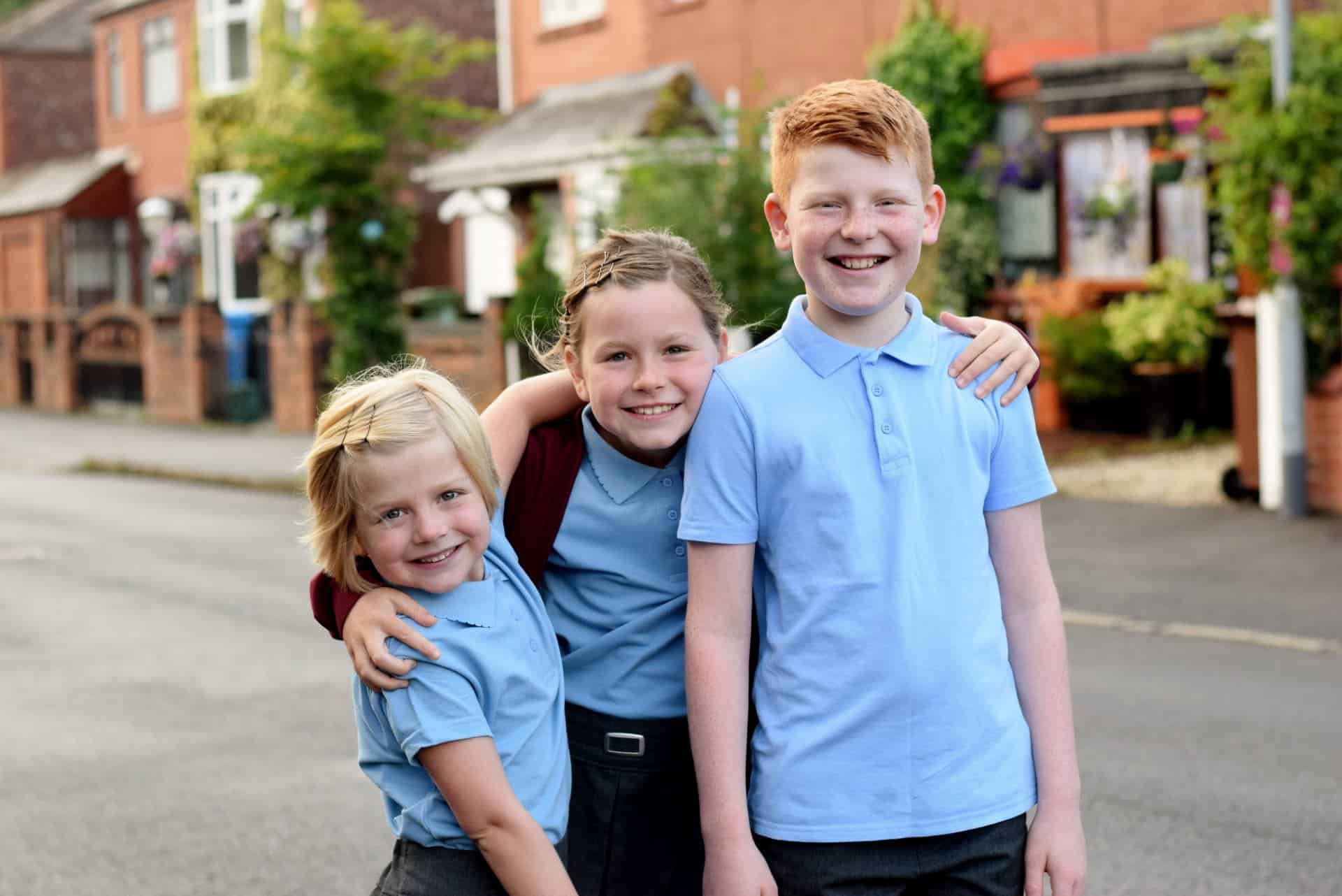 Three kids in school uniform - wearing blue polo shirts and burgundy cardigans