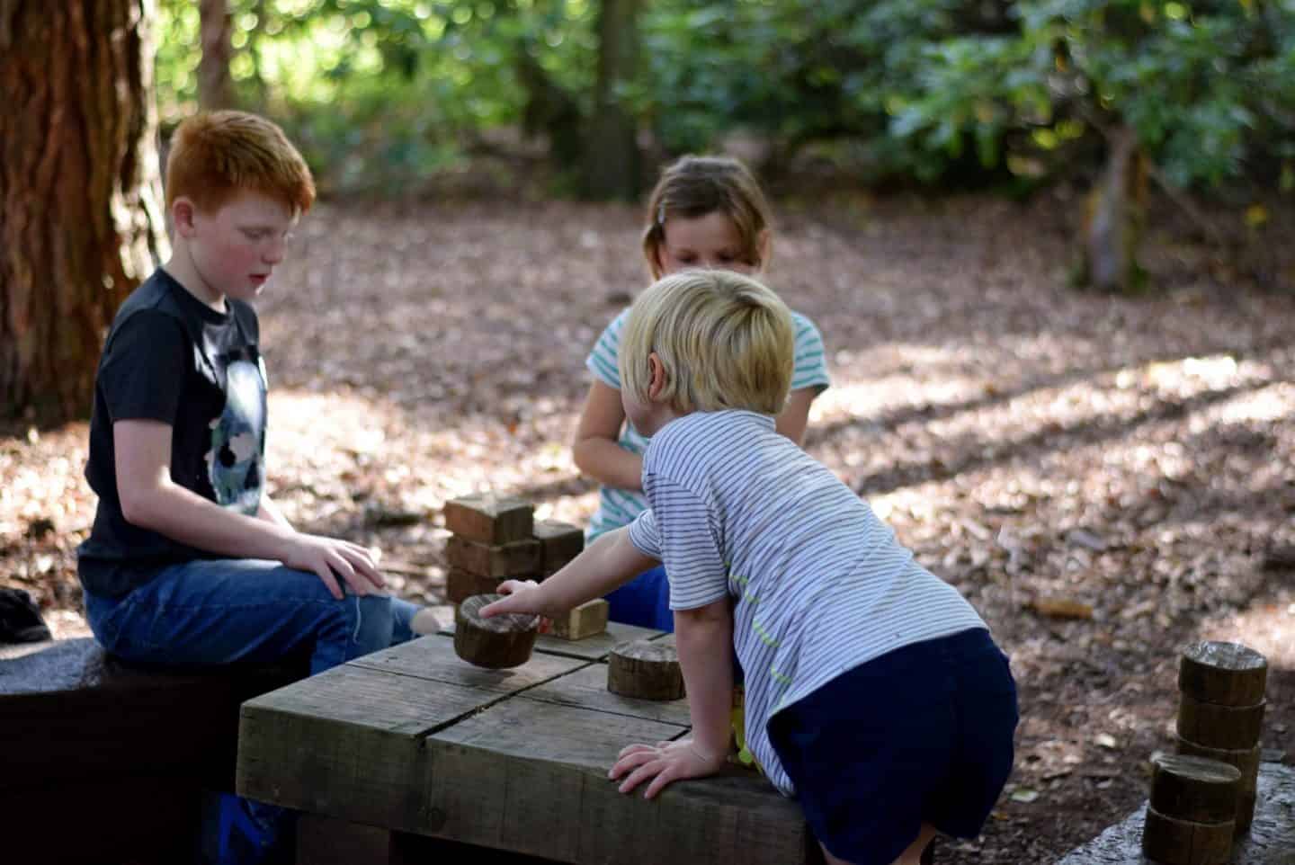 Children playing a giant wooden game of naughts and crosses in the forest