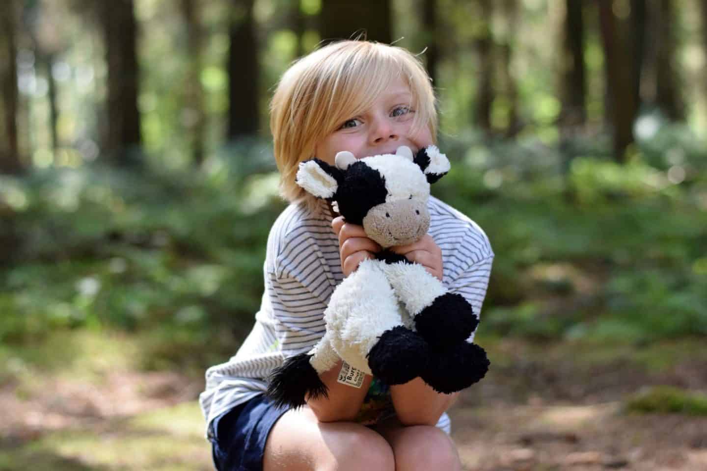 Little girl with cuddle jellycat cow in the forest
