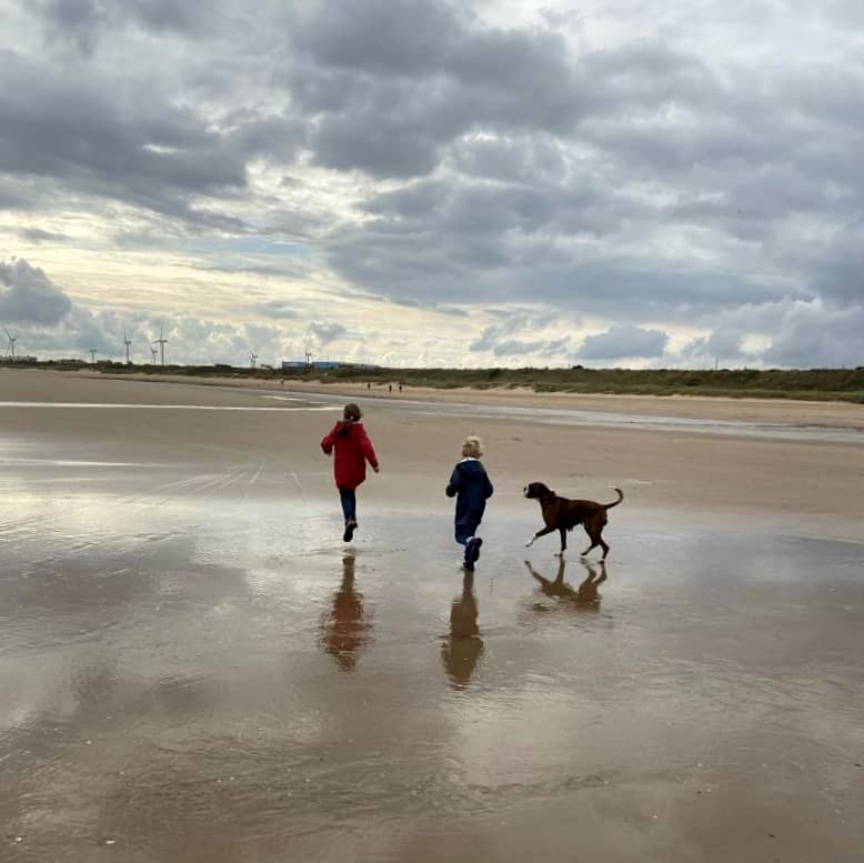 children running on the beach in Bridlington with a boxer dog during the autumn months