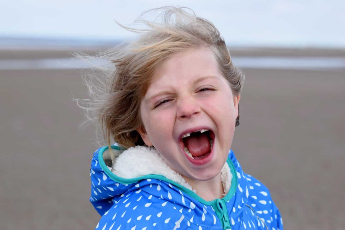 Little girl shrieking with joy on a windy beach wearing a sherpa lined hooded jacket