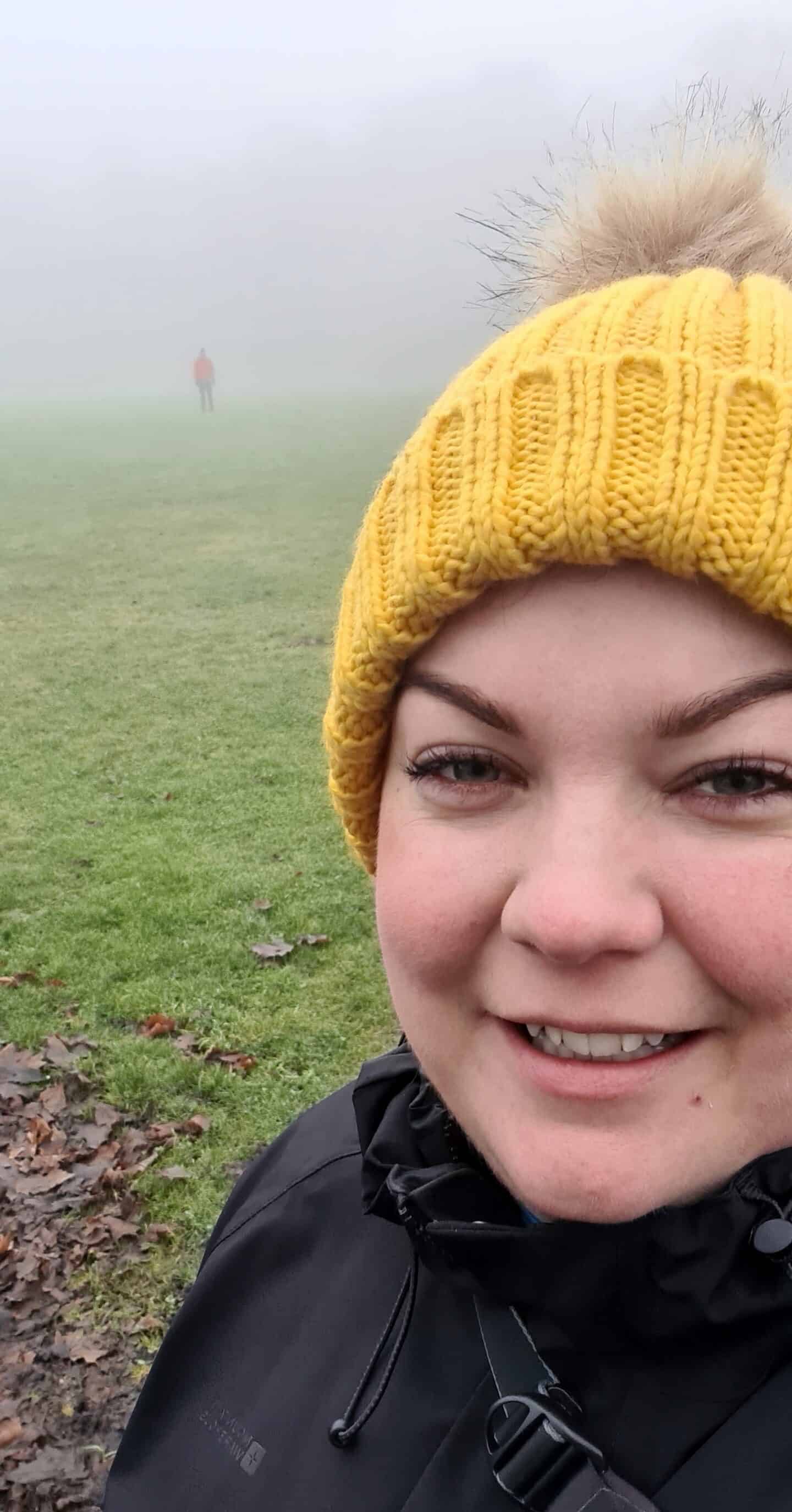 Colette wearing a bright yellow woolly hat, with Dave in the distance obscured by fog