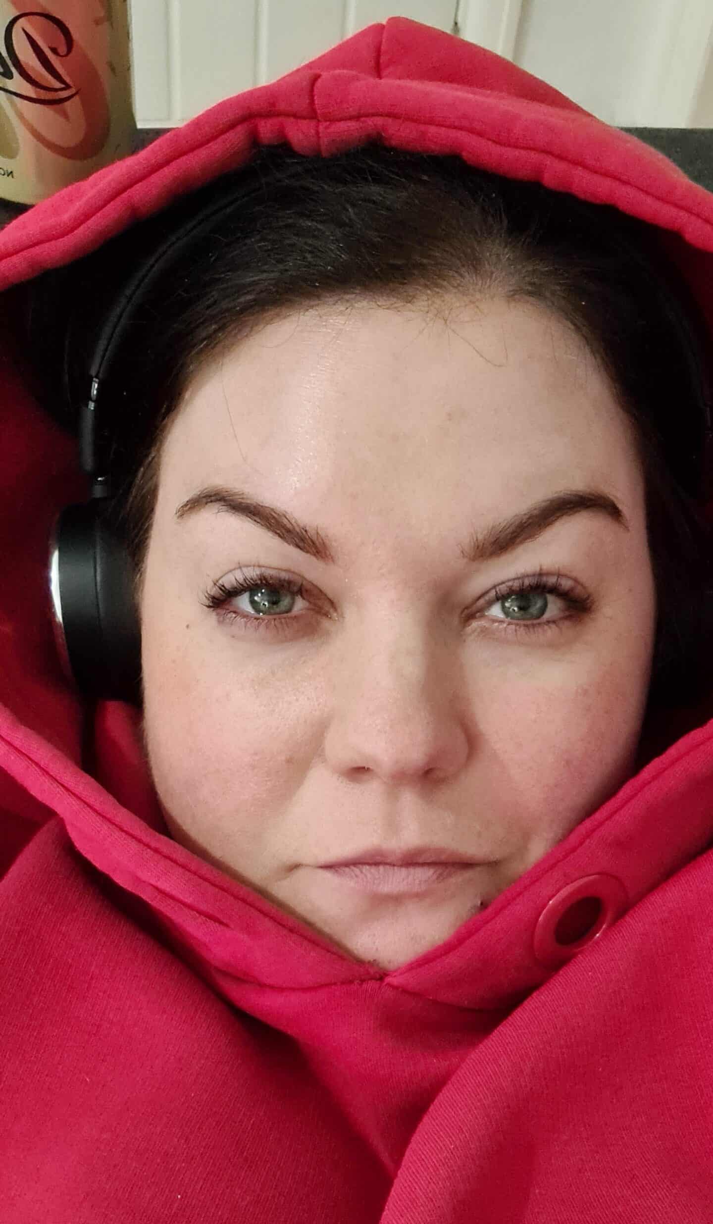 Colette wearing headphones and a big red hoodie, relaxing on the sofa