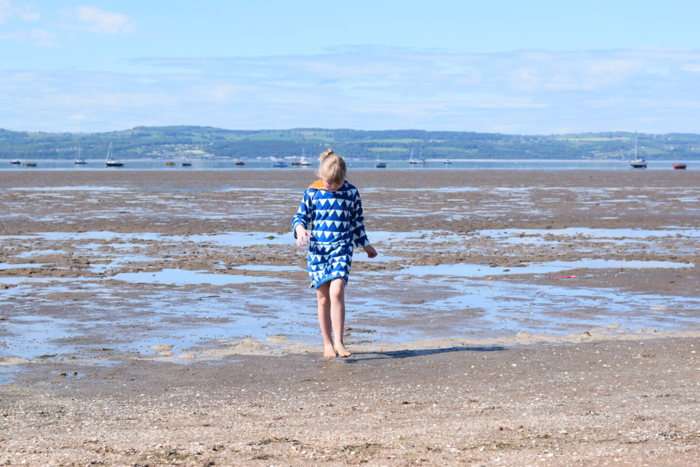 Little girl on the beach in West Kirby with Wales in the background and boats bobbing on the water