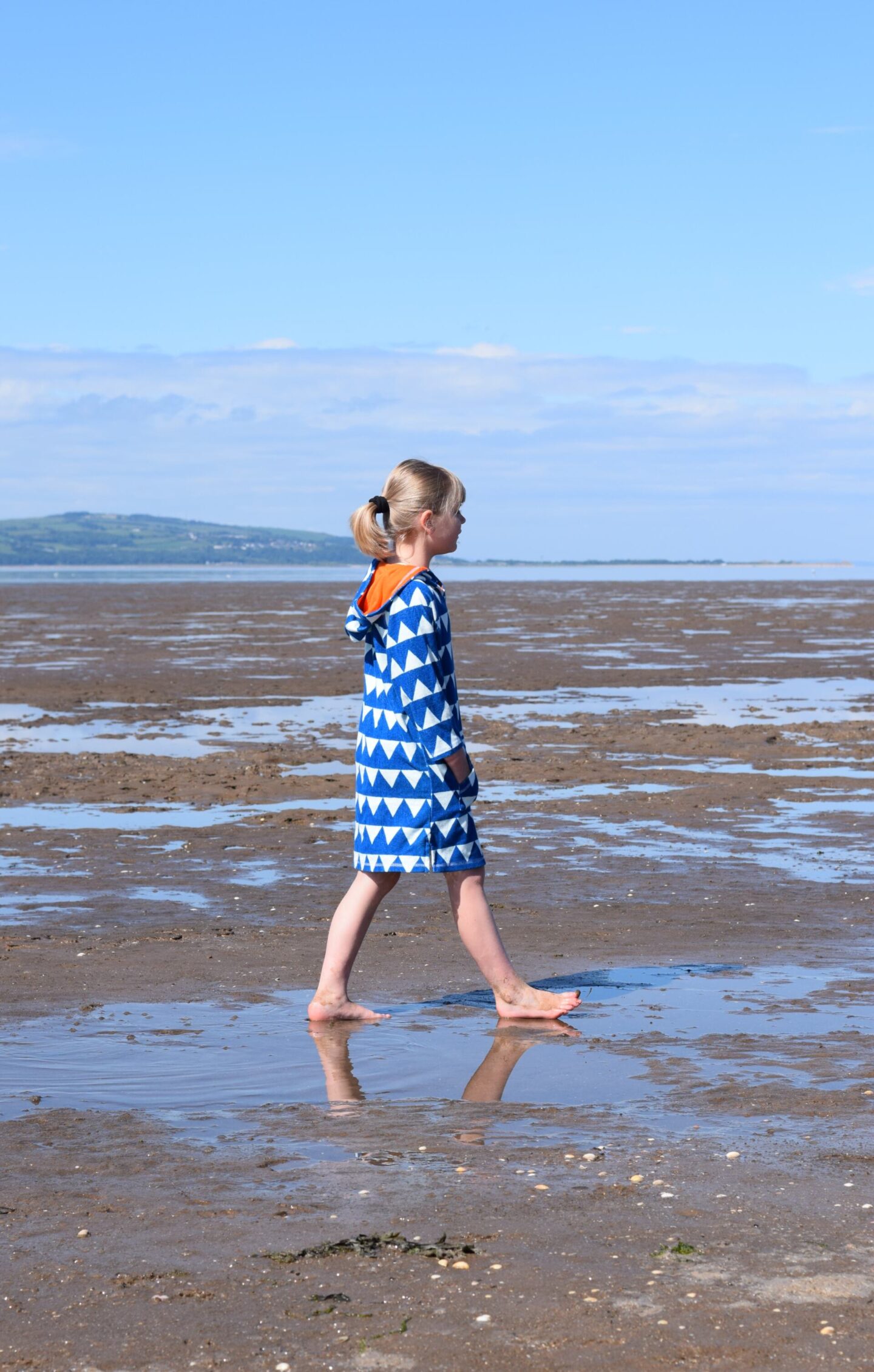 Little girl walking across the sand, paddling in puddles