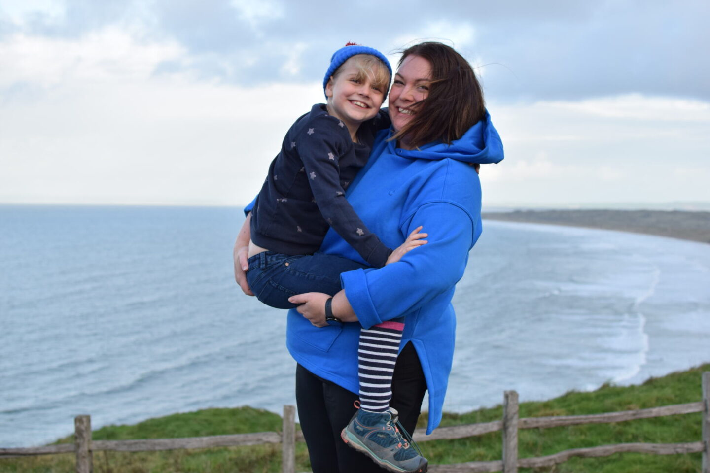 Amy and Colette having a cuddle and smiling to the camera with the beach in the background