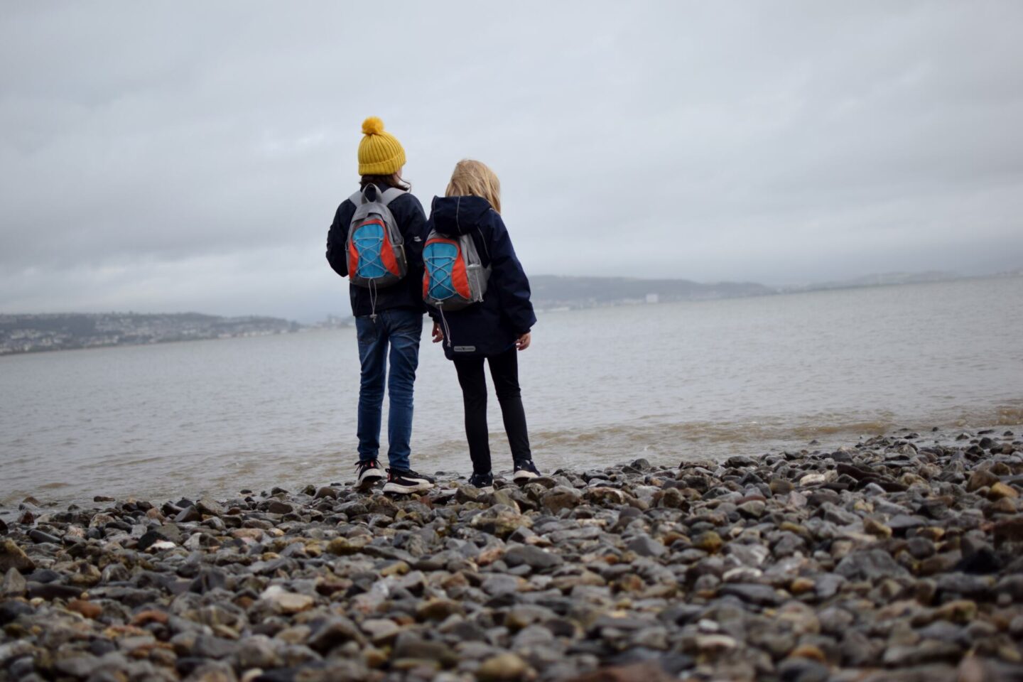 Girls standing on the stony beach in Mumbles, taking in the view on a misty October day