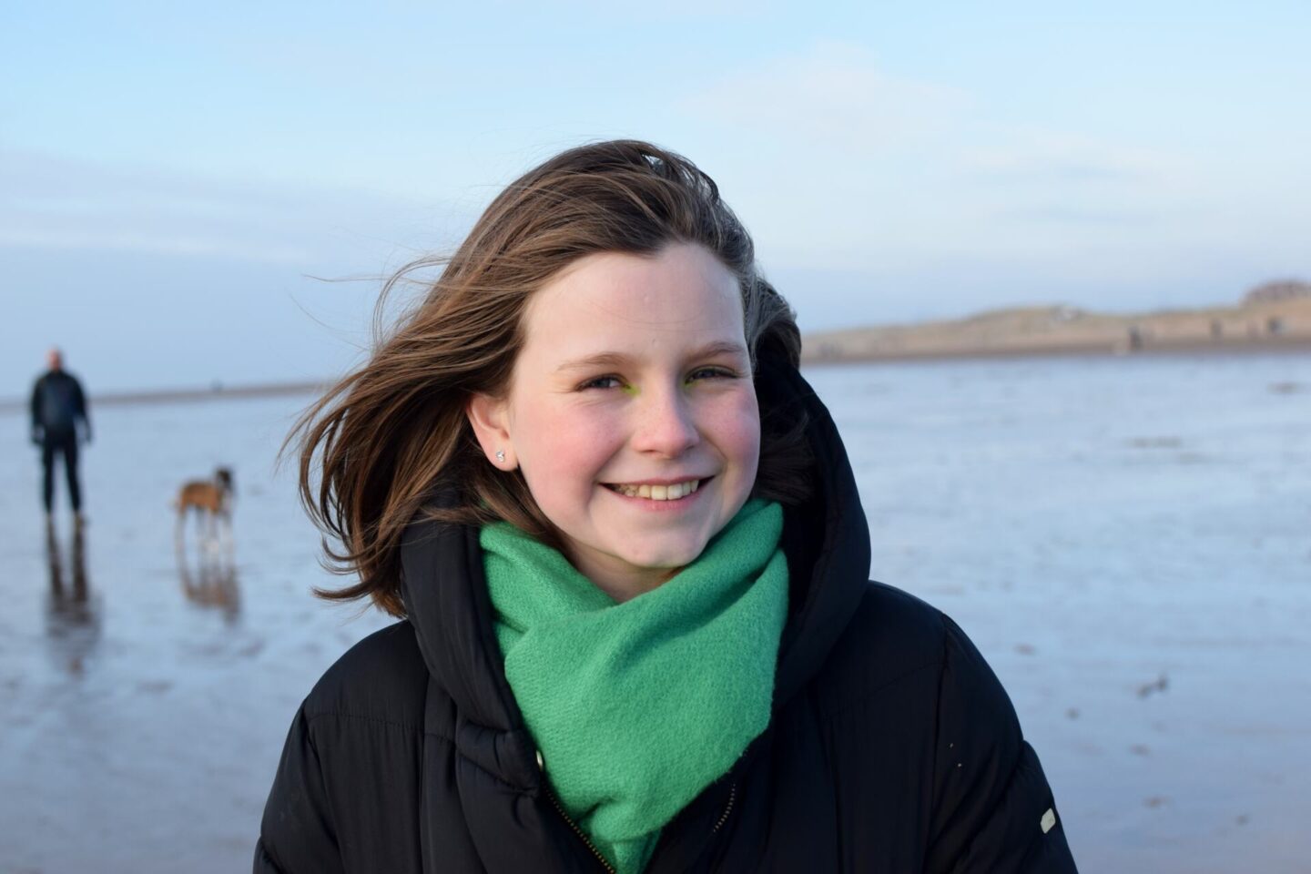 Chloe's hair is blowing in the wind as she looks directly at the camera and smiles broadly - she is wearing bright green eyeshadow on the inner corners of her eyes to match her green scarf.
