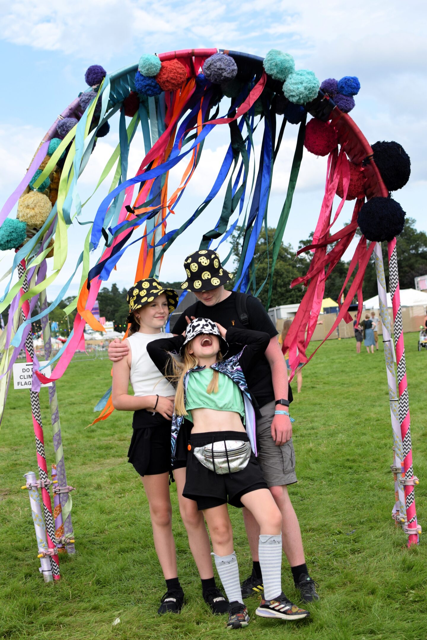 Ben, Chloe and Amy sporting bucket hats standing under an arch decorated with pom poms and streamers at CBS 2023
