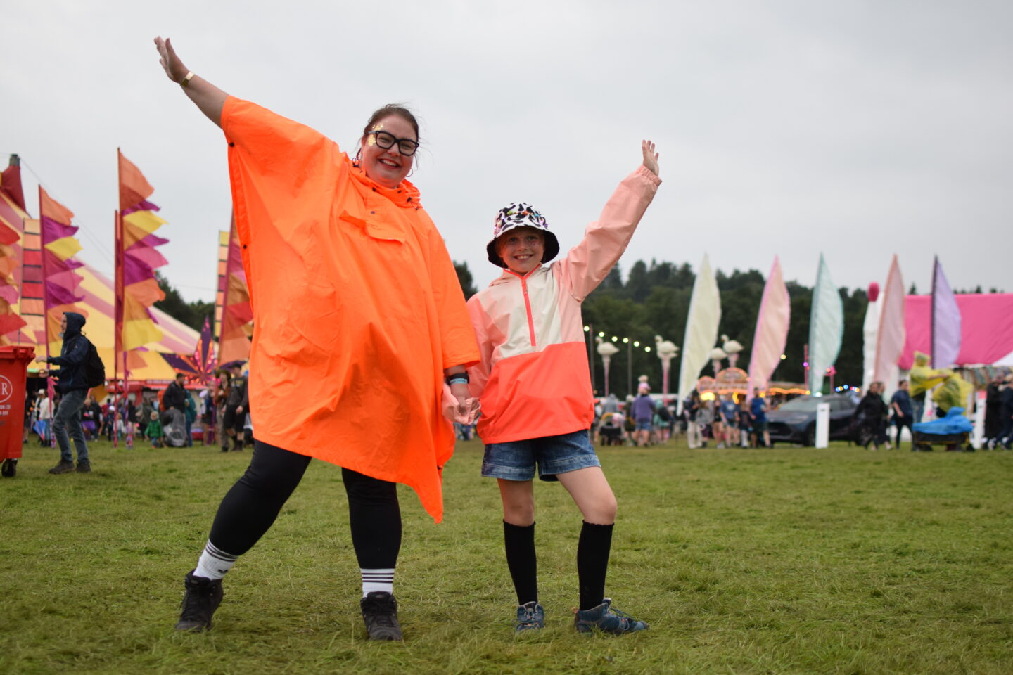 Colette wearing a neon orange poncho and Amy in a bright waterproof coat at Camp Bestival Shropshire