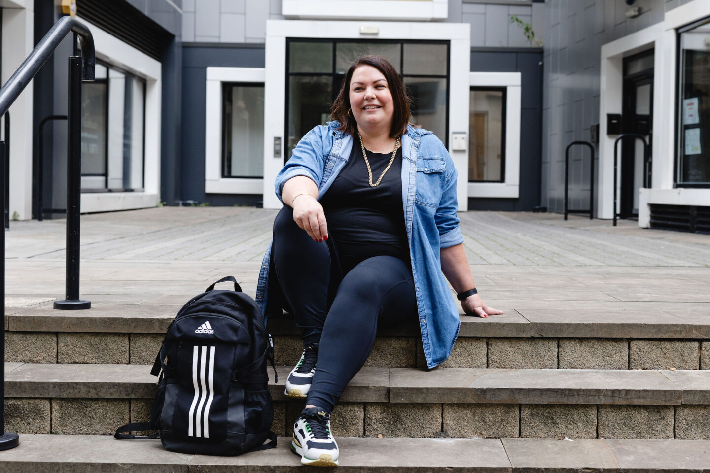 Colette B sitting on the steps with her adidas bag at her feet and smiling at the camera